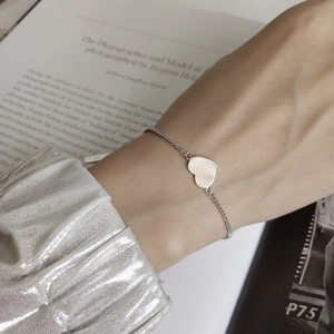 Detailed view of an S925 silver heart charm bracelet on a wrist with silk cuff styling