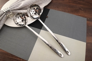 Close-up of stainless steel slotted spoons with leaf pattern handles on a dining mat