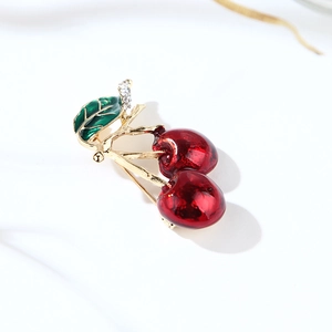 Macro shot of red cherry brooch with gold stem, green leaves and sparkling rhinestones
