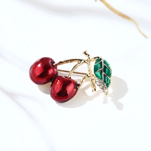 Detailed close-up of a red cherry brooch with crystal leaf on white fabric texture