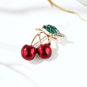 Close-up of red enamel cherry brooch with green leaves and rhinestone accents on white fabric