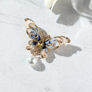 Détail d'une broche papillon en émail bleu avec pierre jaune et pendentif en perle