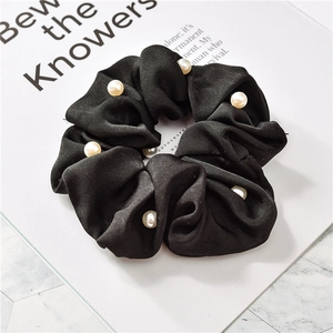 Detail of black satin scrunchie featuring white pearl embellishments and golden trim