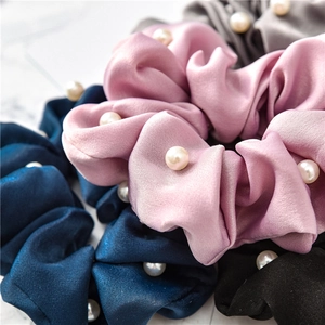 Macro detail of satin scrunchies with white pearl beads on marble surface
