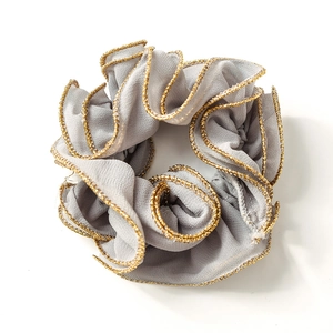 Grey large scrunchie with metallic gold edge trim and pleated fabric texture on white background
