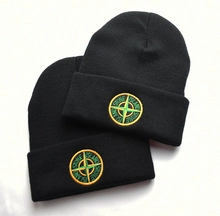 Close-up of black knit beanie featuring detailed circular compass logo embroidery on the cuff