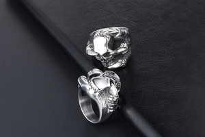 Macro view of two gothic silver skull claw rings on black leather texture