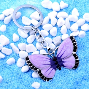 Detail view of purple enamel butterfly keychain with black rhinestones on blue sand