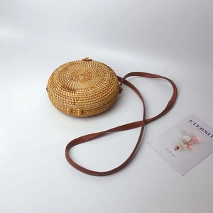 Handcrafted round rattan crossbody bag with brown leather strap on white background