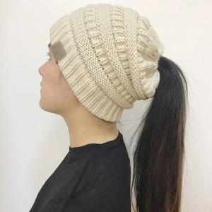Close-up of cream knit ponytail beanie showing cable stitch texture and top opening