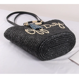Detail of black straw tote with Off Duty text, circle handles, and colorful tassel