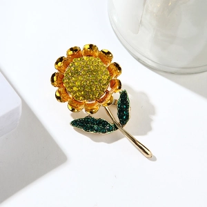 Golden sunflower brooch with vibrant yellow and green rhinestones on white surface