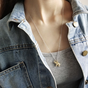 Detailed close-up of a golden elephant pendant necklace worn over a denim jacket