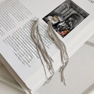 Detail shot of silver tassel earrings with zircon stones on an artistic book background