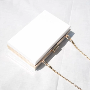 Detail of white acrylic clutch bag with gold metal frame and delicate chain strap