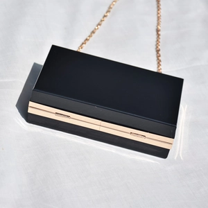 Macro shot of matte black clutch featuring gold metal frame and long chain strap
