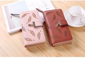 Detailed view of long faux leather wallets with leaf cutout design on a wooden desk