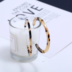 Fashionable leopard print acrylic C-shape hoop earrings displayed on a glass cup