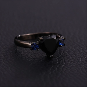 Gothic black gold heart ring with large black zircon and blue accent stones on dark leather