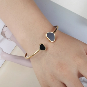 Elegant gold-plated stainless steel open bangle featuring black heart charms on wrist