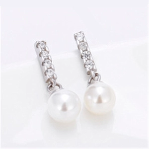 Macro detail of white pearl earrings with sparkling zircon-encrusted silver finish studs