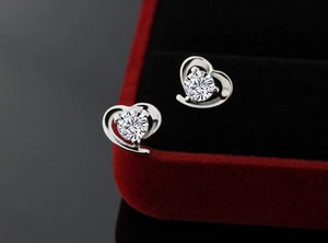 Macro shot of heart-shaped silver earrings with sparkling white zircon in red velvet box
