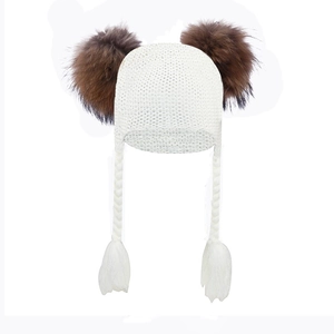 Detail of white knit baby earflap hat with large brown faux fur pom poms and tassels