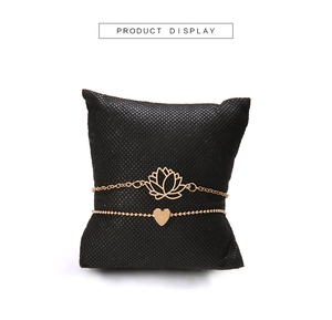 Ensemble de bracelets dorés avec breloques lotus et cœur sur un petit coussin noir
