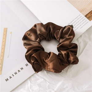 Detail of a smooth coffee brown satin scrunchie styled on a minimalist aesthetic desk