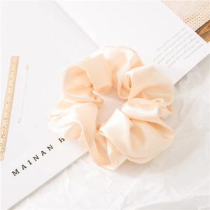 Detail of elegant champagne satin scrunchie with smooth texture next to a wooden ruler