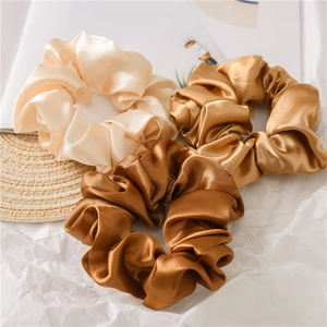 Detailed close-up of three satin scrunchies in cream, champagne, and bronze earth tones