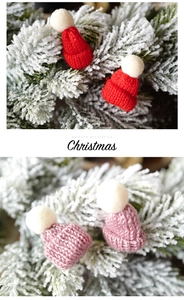 Close-up of mini knitted Christmas hats in red and pink colors on frosted pine needles