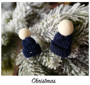 Mini navy blue knitted Christmas hats with white pom-poms on snow-covered pine branches