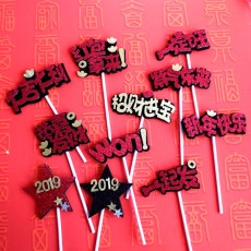 Macro shot of red glitter acrylic cake toppers with Chinese New Year blessings on red background
