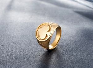 Detailed side view of a gold-toned spade signet ring on a dark textured surface