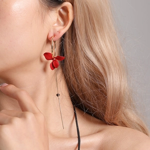 Boucles d'oreilles pétales asymétriques à pampilles dorées et rouges portées par un modèle