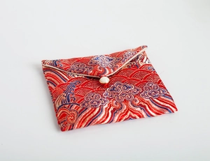 Macro detail of red silk brocade jewelry pouch with gold cloud pattern and pearl closure