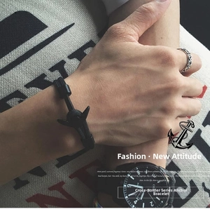 Macro detail of men's black woven nautical bracelet with matte metal anchor clasp