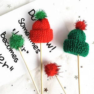Close-up of mini knitted red and green hats with pompoms for Christmas cake toppers