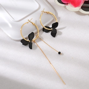 Détail de boucles d'oreilles pendantes asymétriques dorées avec fleurs noir mat
