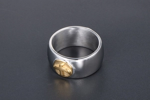 Macro shot of silver titanium steel ring with a round golden embossed eagle cross design