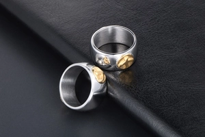 Detail of wide stainless steel rings with gold embossed bird motifs on dark leather