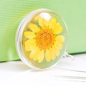 Macro shot of a handmade glass pendant featuring a yellow dried daisy with silver metal rim