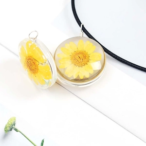 Close-up of handmade round glass pendant featuring a real yellow dried flower and black cord