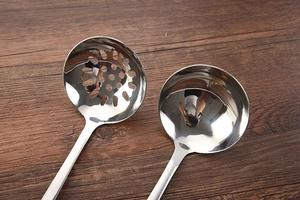Polished stainless steel soup ladle and slotted spoon set on dark wood background