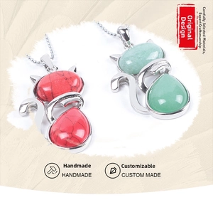 Detail showing handmade cat pendants with pink and green stones on silver chains