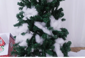 Close-up of white artificial fiber fake snow flakes on green Christmas tree branches