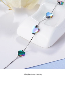 Close-up of minimalist box chain bracelet with iridescent heart charms on white ceramic