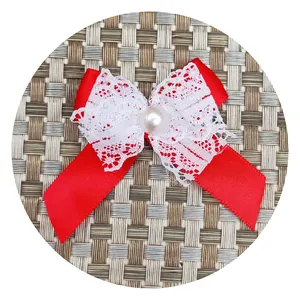 Red ribbon bow accessory with white lace layers and a white pearl center on textured surface