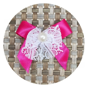 Detail of rose red satin bow with white lace trim and centered pearl on woven background